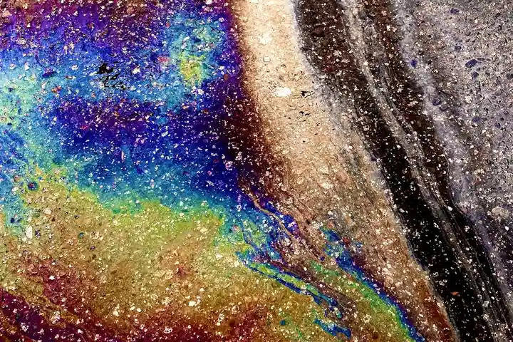 Close-up abstract texture of multicolored oil-like swirls in gold, purple, blue, and green