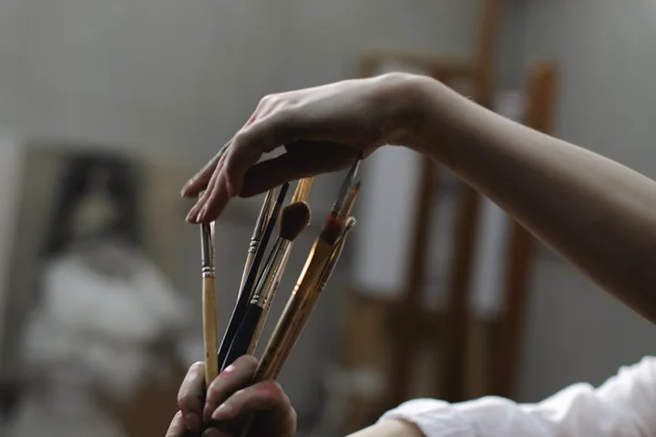 Close-up of a hand holding several painter's brushes, ready for cleaning.
