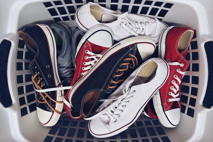Assorted sneakers in a white laundry basket, featuring red, white, navy, and gray canvas shoes.