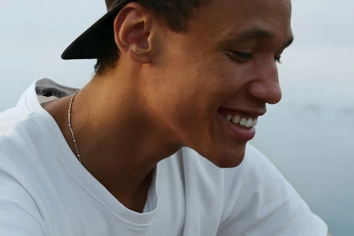 Smiling person wearing a backward baseball cap and a white shirt