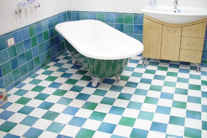 White clawfoot bathtub in a bathroom with teal and blue tiled floor and walls, with a wooden vanity to the right.