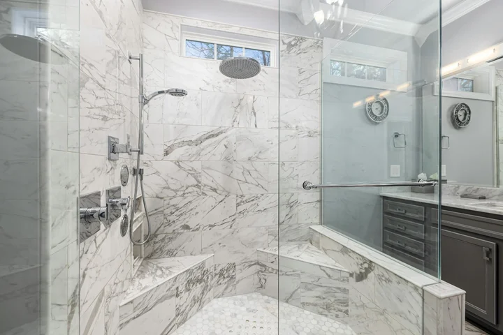 Interior of a glass-enclosed marble shower with a built-in bench and a dark vanity, showcasing polished surfaces