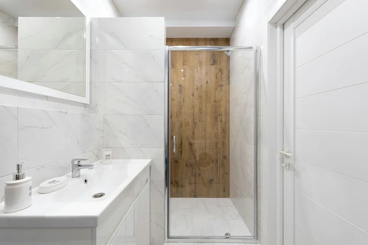 Bright bathroom with white tiles, a glass shower enclosure, and a white vanity.