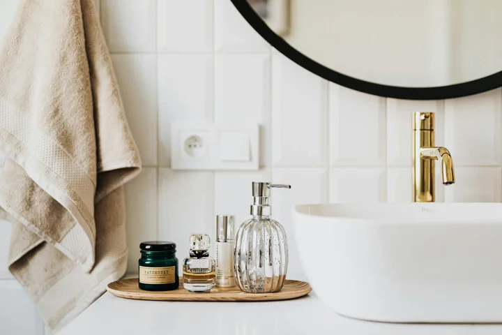 Minimalist bathroom vanity with a round mirror, a beige towel, and a tray of cosmetic bottles beside a white sink.