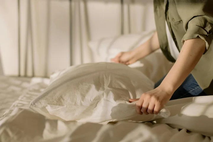 Person smoothing a white bedsheet on a bed to prevent wrinkles