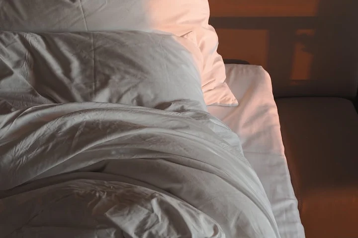 Crinkled white sheets and a gray blanket on a bed
