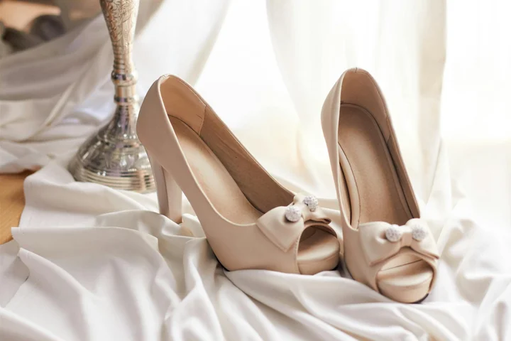 Beige peep-toe high-heeled shoes with bows resting on white fabric