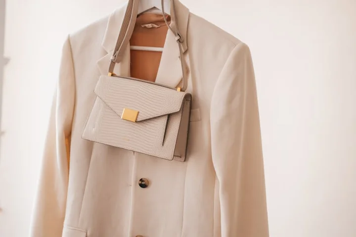 Beige trench coat hanging on a hanger with a small matching beige handbag.