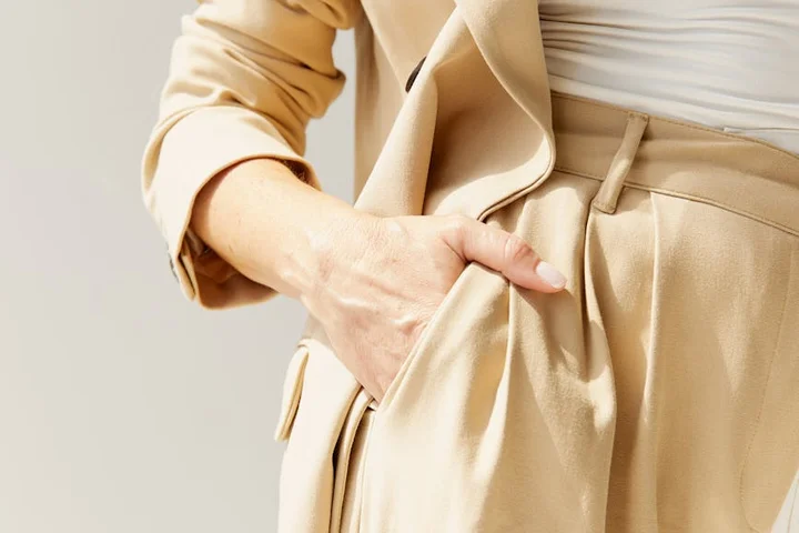 Close-up of a beige coat and pants with a hand in the pocket