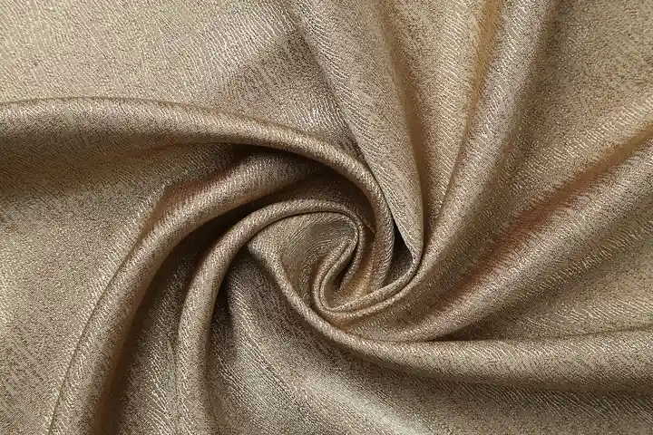 Close-up of beige fabric with swirling folds and a subtle sheen.