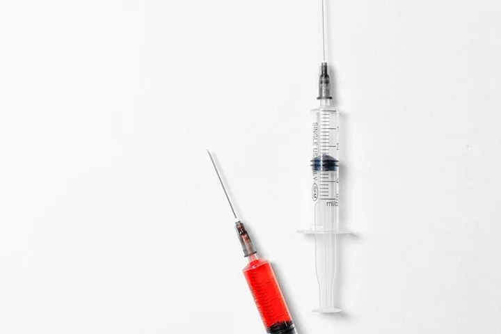 Close-up image of a syringe with red liquid and a needle on a white background, used to symbolize initial precautions in blood stain care.