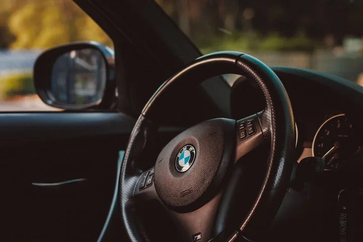 Close-up of a car's steering wheel inside a dimly lit cockpit, with the BMW emblem visible.