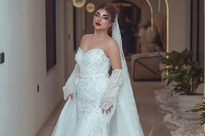 Woman in a white lace wedding dress and veil standing indoors