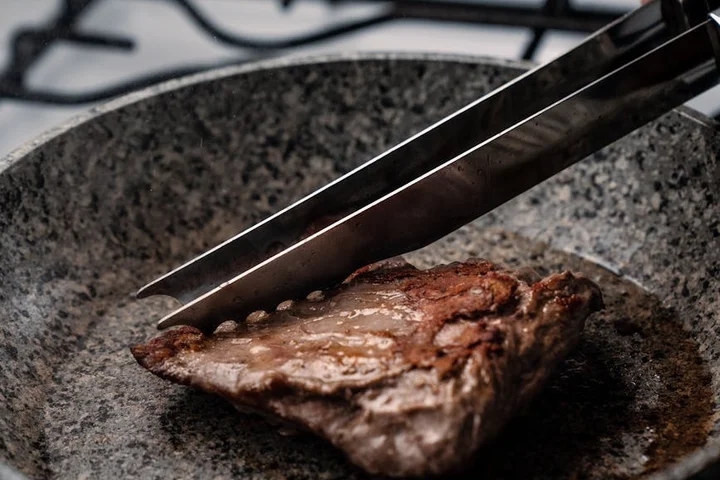 Burnt piece of food stuck to a pan with tongs resting above, illustrating cleaning a non-stick surface