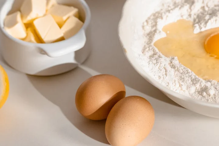Butter cubes, eggs, and a bowl of flour on a kitchen counter