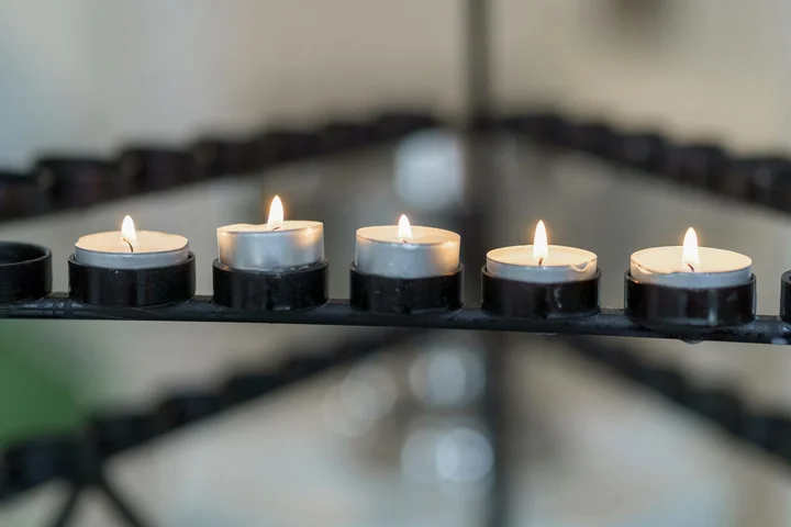 Close-up of tealight candles in black round holders on a metal rack, with a blurred background.