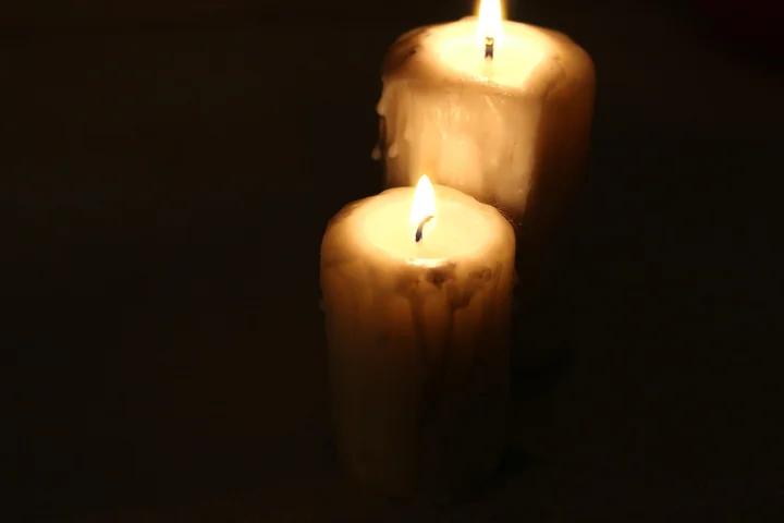 Two lit candles casting a warm glow in a dark setting, with melted wax around their bases.