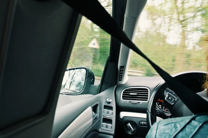 Interior of a car with a seat belt draped across the front seats and a view of the dashboard and steering wheel.