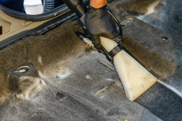 Close-up of a gloved hand using a vacuum attachment to remove dog hair from a car carpet.