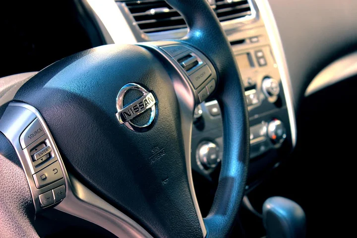 Close-up of a Nissan steering wheel inside a car, with the dashboard and controls in the background.