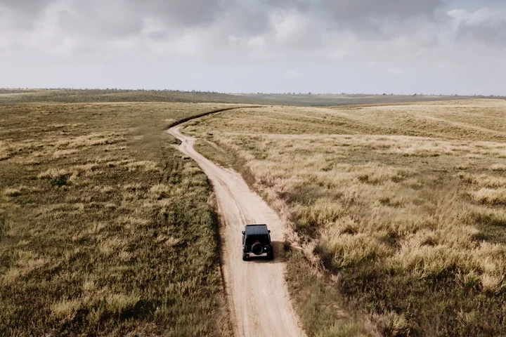 An SUV driving along a dusty dirt road through a wide grassy landscape, illustrating the need for a go-to stain toolkit for on-the-go messes.