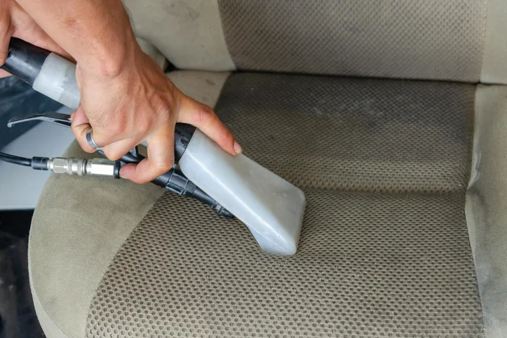 Person using a handheld upholstery cleaning device on a beige fabric car seat