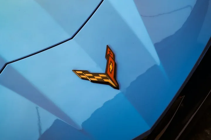 Close-up of a blue car hood featuring an orange Corvette emblem