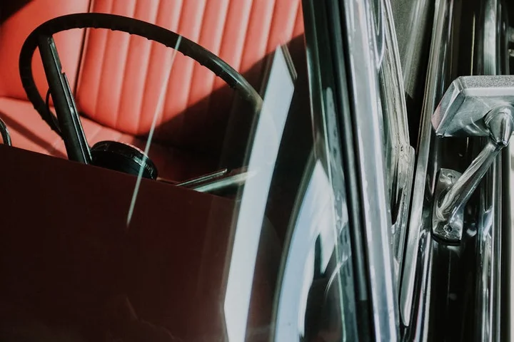 Close-up of a car interior featuring red upholstery and a steering wheel, with glass windows visible