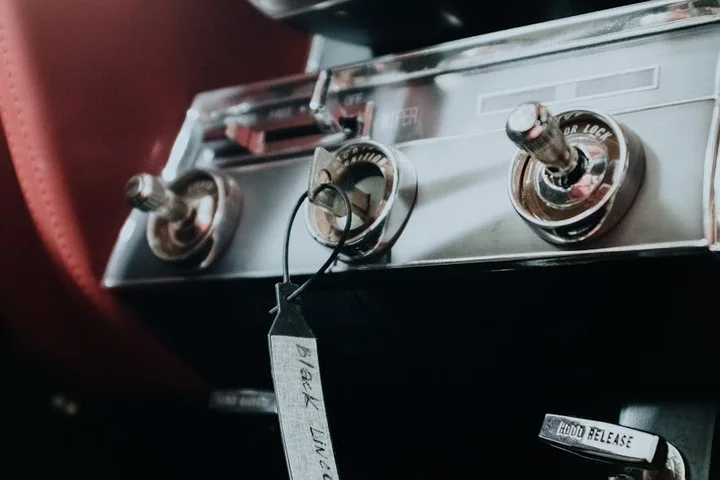 Close-up of a vintage car dashboard with chrome knobs and a hanging tag.