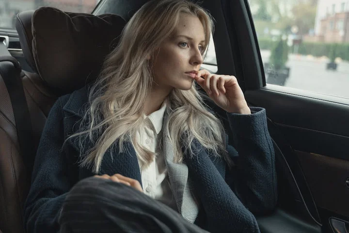 Woman seated in the back of a car, looking thoughtfully out the window.