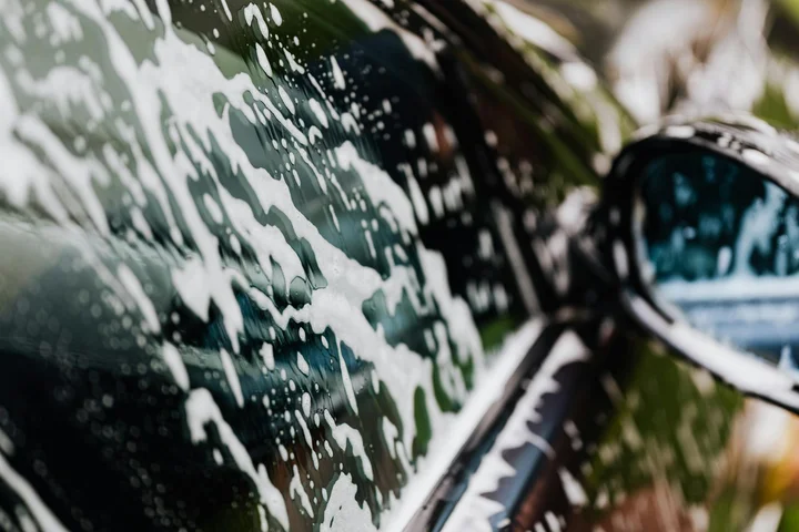 Close-up of a car window with soap suds, emphasizing careful cleaning to protect the paint and exterior surfaces during adhesive residue removal.