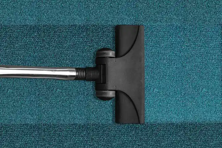 Close-up of a carpet cleaning wand on a blue carpet, illustrating cleaning equipment.
