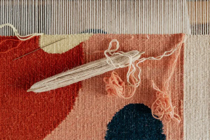 Close-up of a red patterned carpet showing loose fibers and exposed weave with frayed threads, illustrating material concerns.