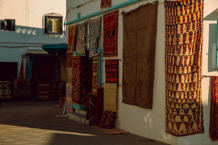 Display of colorful rugs hanging along the exterior wall of a textile shop.