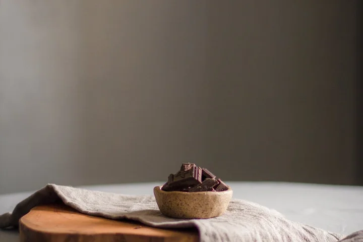A small chocolate tart with chocolate chunks on a light linen cloth, resting on a wooden surface.