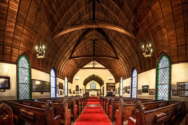 Interior of a church with a wooden vaulted ceiling, rows of pews, and stained glass windows.