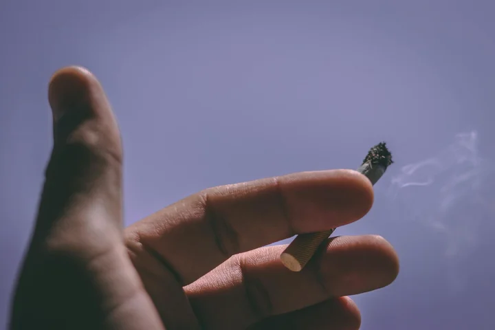 Close-up of a hand holding a cigarette against a blue sky.