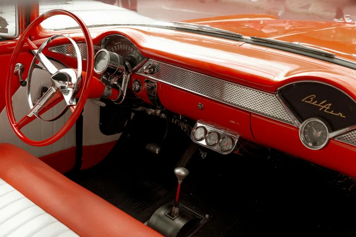 Classic red and white vintage car interior with chrome dashboard and steering wheel.