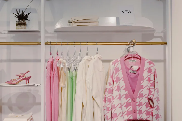 White closet with pastel-colored clothing on hangers, including a pink and white patterned cardigan on the right.