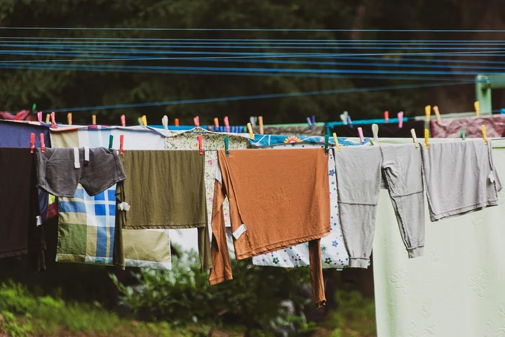 Colorful garments and towels hanging on a clothesline outdoors to dry, with clothespins and green scenery.