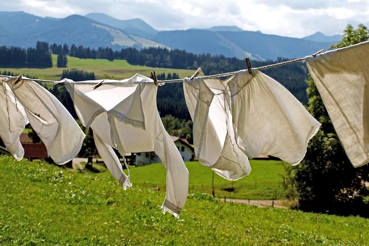 Laundry hanging on a clothesline in a sunny rural field with mountains in the background.