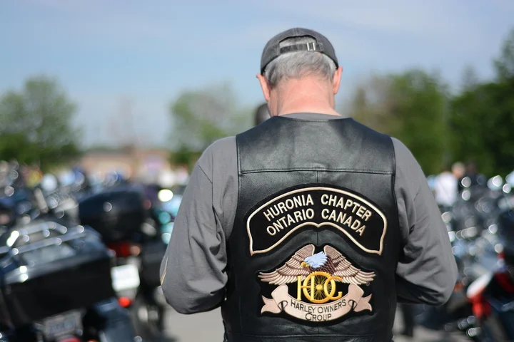 Back view of a man wearing a black leather vest with a Harley Owners Group patch at a motorcycle gathering.