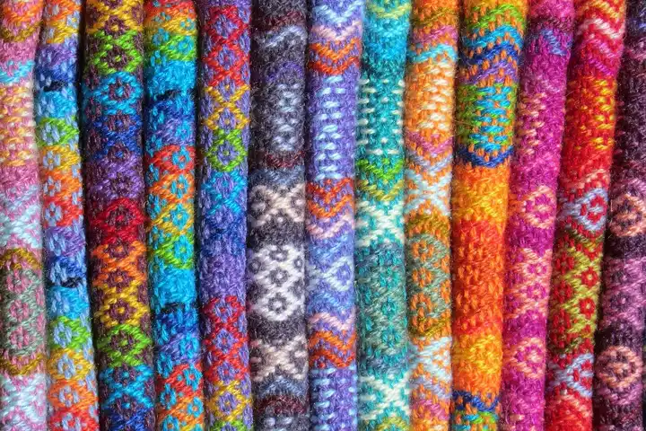 Rows of brightly colored woven fabric rolls with intricate geometric patterns and rich textures.