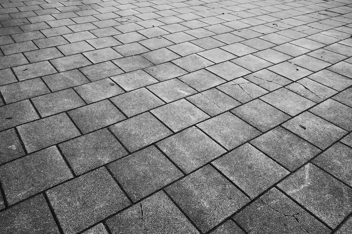 Monochrome image of a gray concrete paver patio with square interlocking blocks.