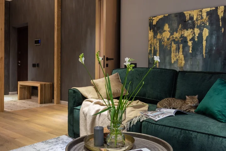 Green velvet sofa with cushions in a modern living room, coffee table with vase, and abstract wall art.