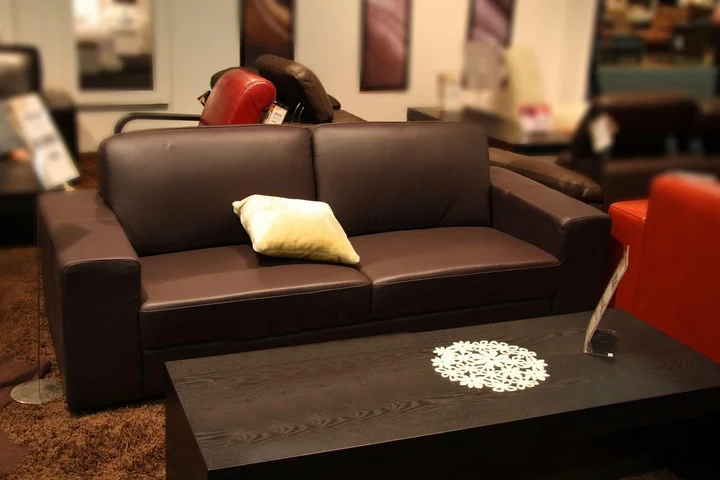 Dark brown sofa on display in a furniture showroom with a black coffee table in front and a decorative pillow