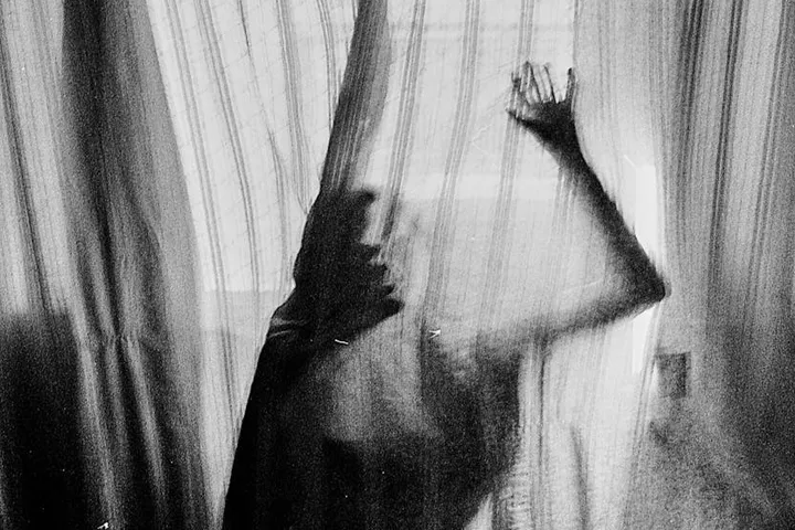 Silhouette of a person pressed against a sheer curtain with light behind