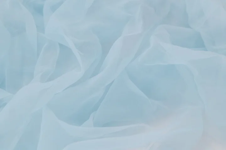 Close-up of light blue, sheer fabric with soft folds, representing delicate textiles.
