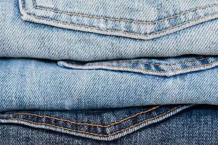 Stacked blue denim jeans in varying washes, illustrating common fabric stains and the role of cleaners.