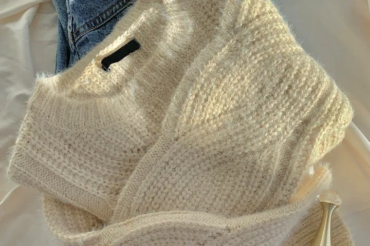 A white knit sweater and blue jeans laid flat, illustrating fabric care steps ahead of stain treatment.